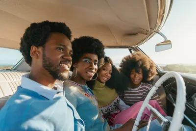 A beautiful family of four nested in the front seat of a retro car on a sunny day.